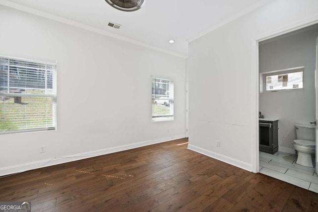 unfurnished bedroom with hardwood / wood-style flooring, ornamental molding, multiple windows, and visible vents