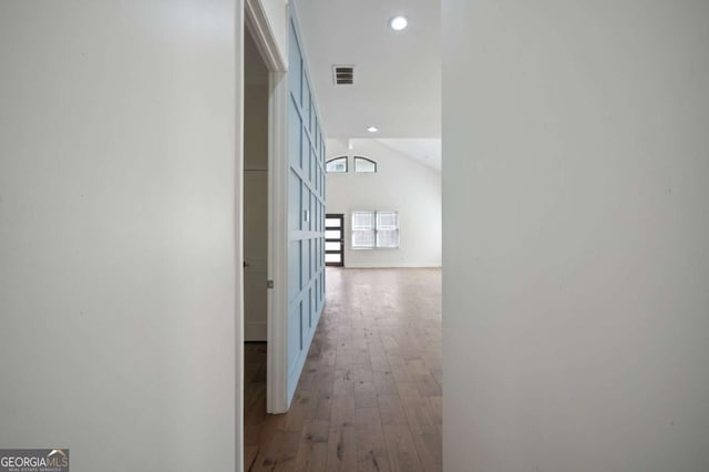 hall featuring light wood-type flooring, baseboards, lofted ceiling, visible vents, and recessed lighting