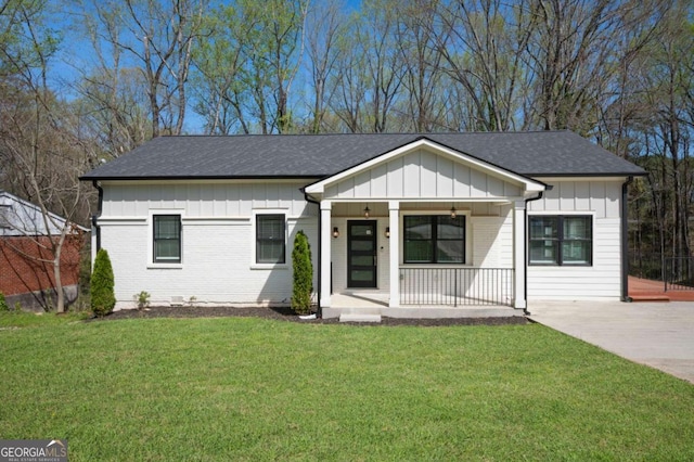 view of front of house with a front lawn, concrete driveway, board and batten siding, covered porch, and roof with shingles