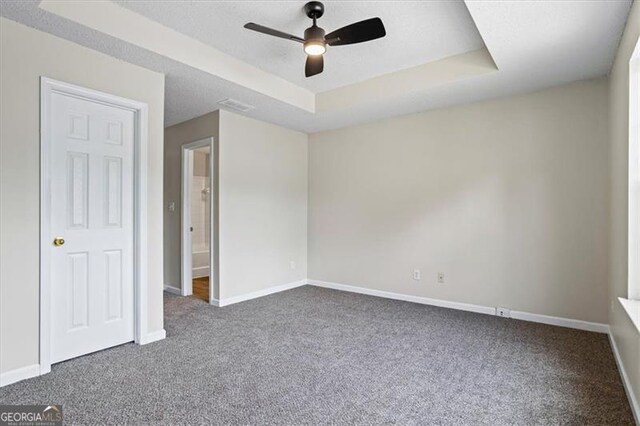 unfurnished bedroom featuring ceiling fan, baseboards, dark colored carpet, and a tray ceiling