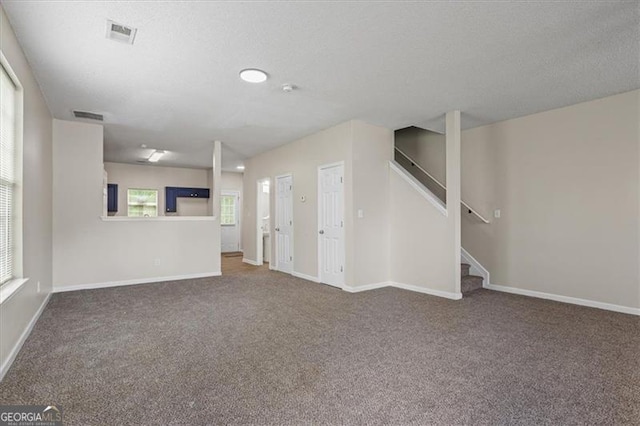 unfurnished living room with stairway, a textured ceiling, and carpet flooring