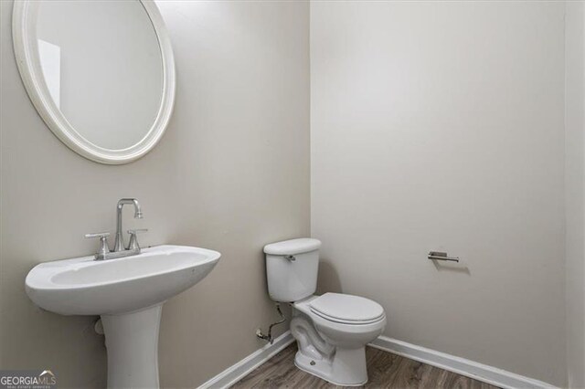 half bathroom featuring toilet, wood finished floors, and baseboards