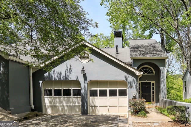 view of front of property with stucco siding, driveway, a chimney, and a garage