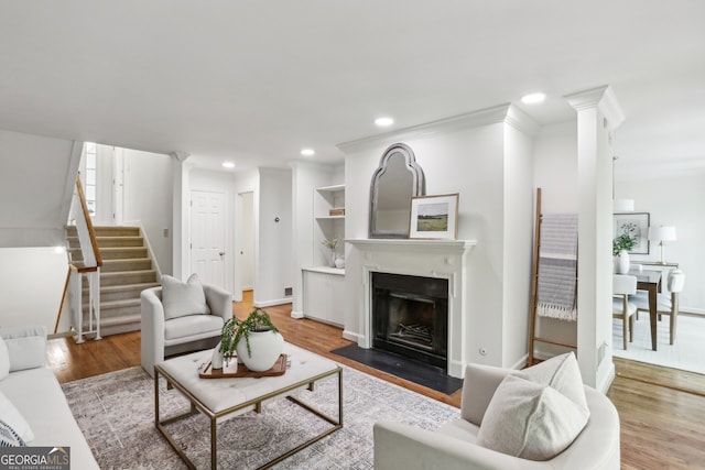 living room with crown molding, wood finished floors, stairs, a fireplace with flush hearth, and recessed lighting
