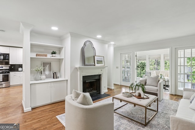living area with a fireplace with flush hearth, light wood finished floors, crown molding, and recessed lighting