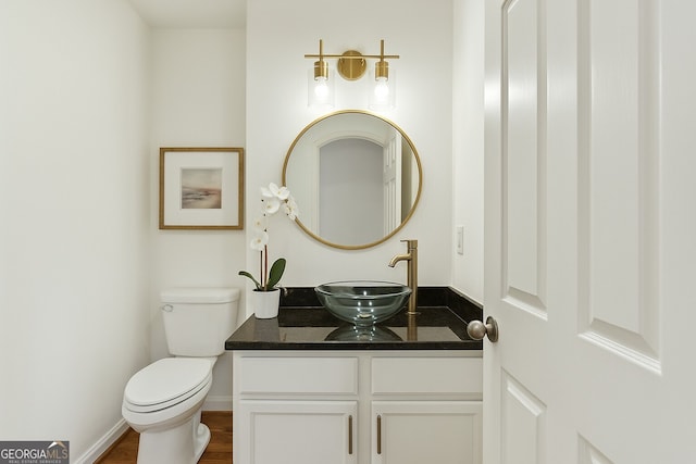 half bath with baseboards, wood finished floors, vanity, and toilet