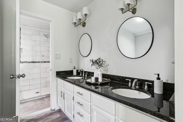 full bathroom with wood finished floors, a sink, double vanity, and a stall shower
