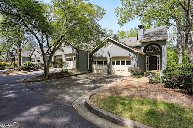 view of front of home featuring a garage, driveway, a chimney, and stucco siding