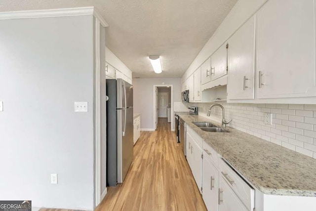 kitchen with a sink, decorative backsplash, light wood-style floors, stainless steel appliances, and white cabinetry