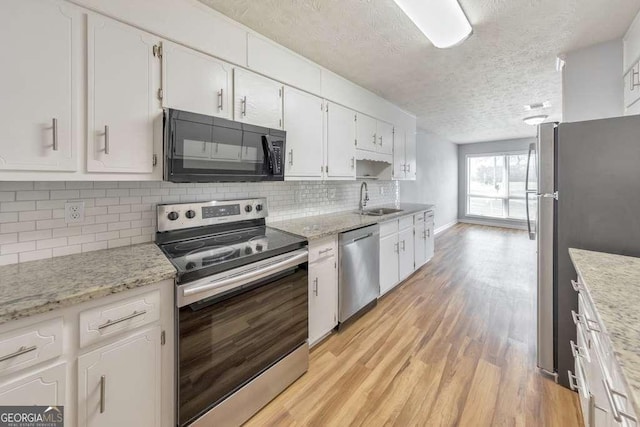 kitchen with stainless steel appliances, a sink, a textured ceiling, light wood-type flooring, and white cabinetry