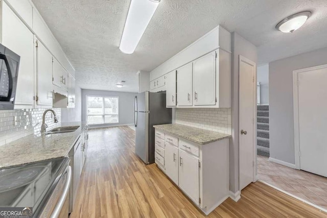 kitchen with stainless steel appliances, a textured ceiling, a sink, and white cabinetry