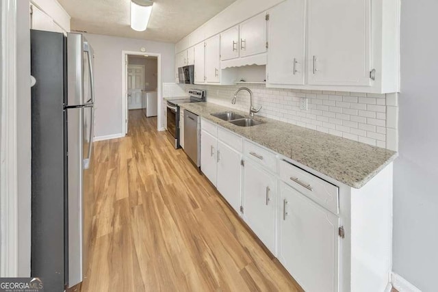 kitchen with tasteful backsplash, a sink, light wood finished floors, white cabinets, and appliances with stainless steel finishes