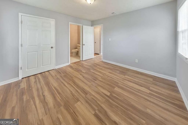 unfurnished bedroom featuring ensuite bath, baseboards, and light wood-style flooring