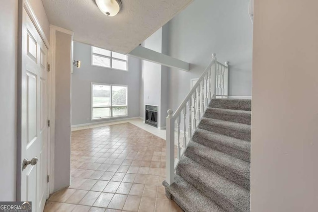 entrance foyer featuring a high ceiling, light tile patterned floors, baseboards, a fireplace, and stairs