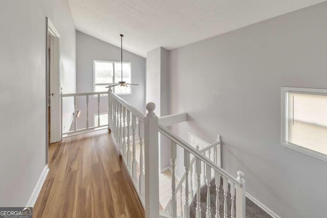 hallway with lofted ceiling, baseboards, wood finished floors, and an upstairs landing