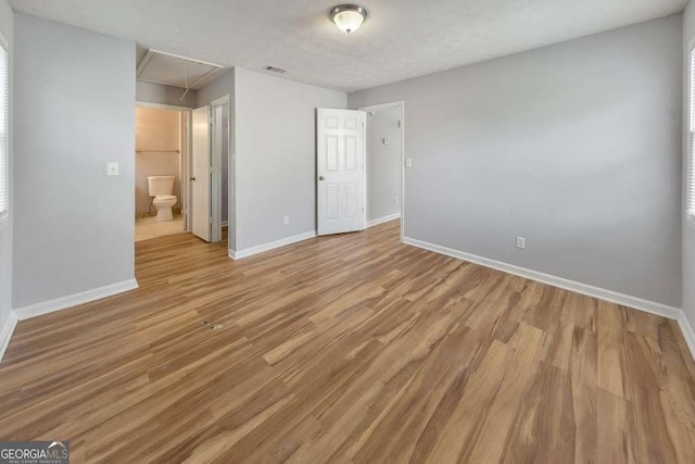 unfurnished bedroom featuring attic access, light wood-type flooring, visible vents, and baseboards