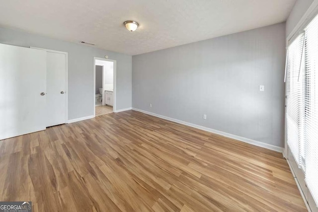 unfurnished bedroom with light wood-style floors, visible vents, baseboards, and ensuite bathroom