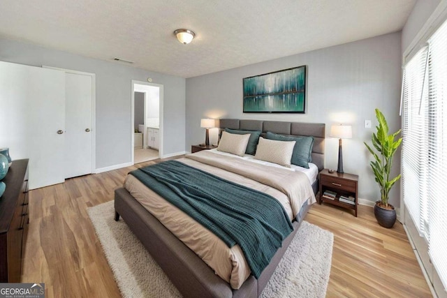 bedroom featuring ensuite bath, baseboards, visible vents, and light wood-style flooring