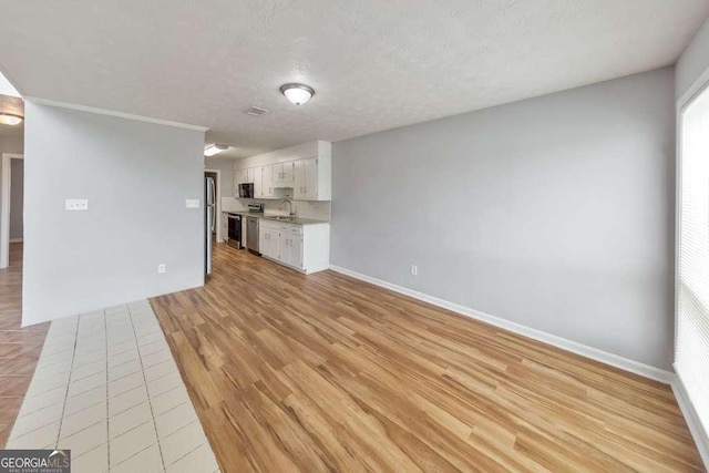 unfurnished living room with a textured ceiling, baseboards, a sink, and light wood-style floors