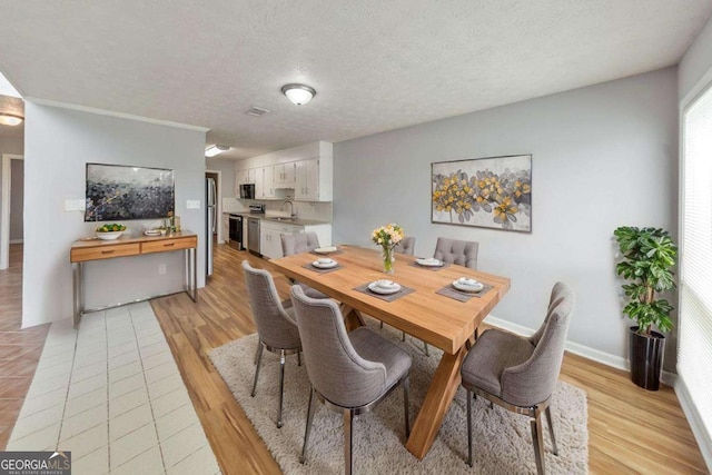 dining space with baseboards, a textured ceiling, and light wood finished floors