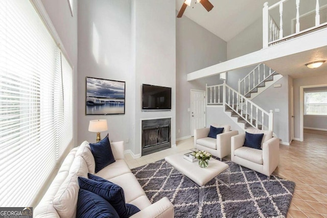 tiled living area with baseboards, high vaulted ceiling, a ceiling fan, stairs, and a fireplace