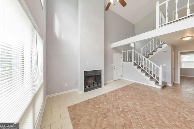 unfurnished living room with stairway, light tile patterned flooring, a fireplace, high vaulted ceiling, and ceiling fan
