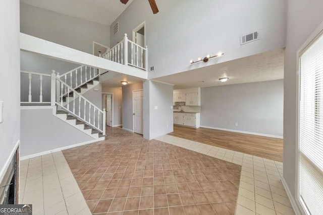 unfurnished living room with a towering ceiling, visible vents, a ceiling fan, light tile patterned floors, and stairs