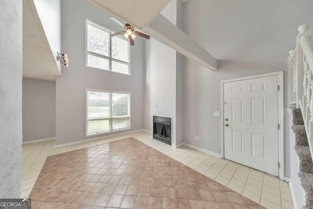 unfurnished living room with a high ceiling, stairway, ceiling fan, a fireplace, and light tile patterned floors