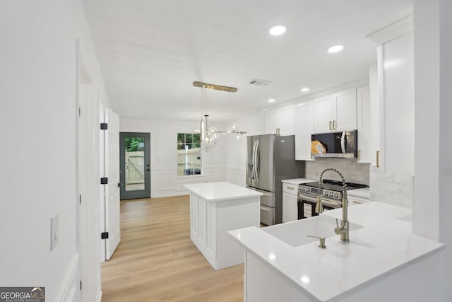kitchen with backsplash, a sink, a peninsula, light wood-style flooring, and appliances with stainless steel finishes