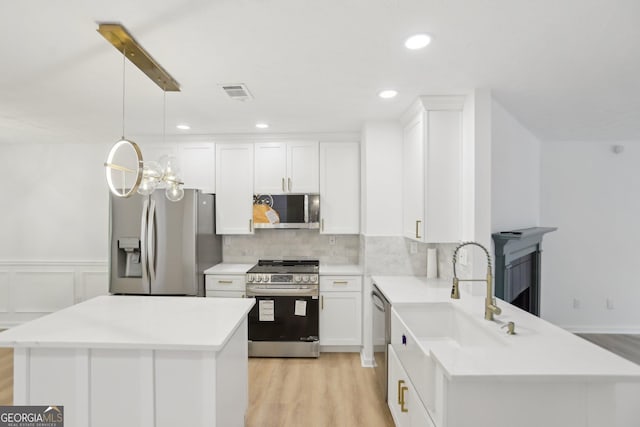kitchen with a center island, light wood-style floors, a notable chandelier, light countertops, and appliances with stainless steel finishes