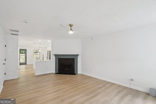 unfurnished living room featuring a fireplace with flush hearth, light wood-style flooring, baseboards, stairs, and ceiling fan