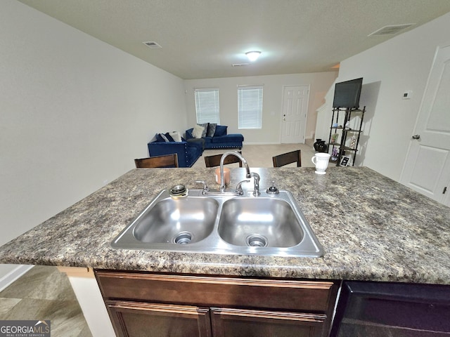 kitchen with a sink, open floor plan, dark brown cabinetry, and dark stone countertops