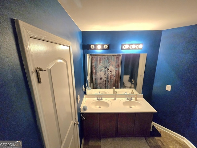 bathroom with toilet, double vanity, and baseboards
