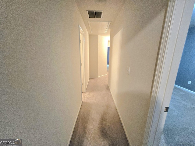 hallway with attic access, carpet, and baseboards