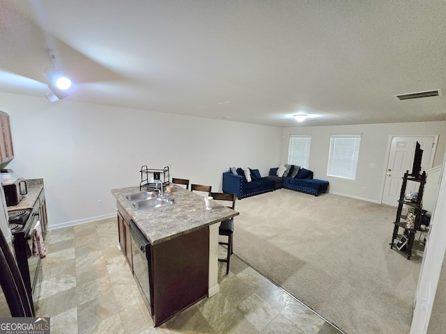 kitchen featuring a breakfast bar area, black / electric stove, a kitchen island with sink, a sink, and baseboards