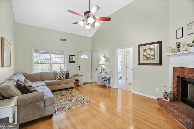 living room with visible vents, a brick fireplace, light wood-style floors, high vaulted ceiling, and a ceiling fan
