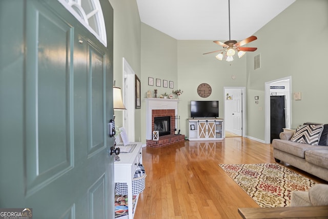 living room with a ceiling fan, visible vents, a fireplace, high vaulted ceiling, and light wood-style floors