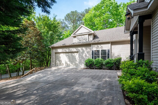 view of side of home featuring concrete driveway, a garage, and roof with shingles