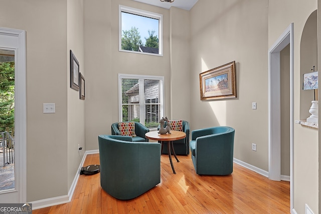 sitting room with a towering ceiling, light wood-style floors, visible vents, and baseboards