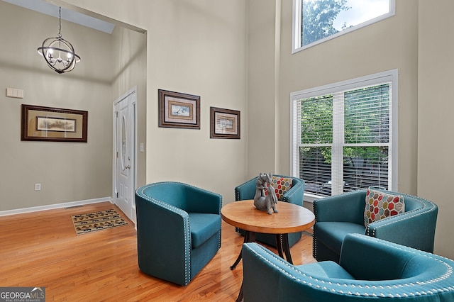 living area featuring light wood finished floors, a wealth of natural light, a high ceiling, and an inviting chandelier
