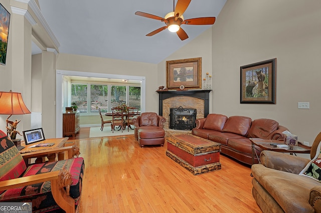 living room featuring ceiling fan, high vaulted ceiling, a stone fireplace, baseboards, and wood finished floors
