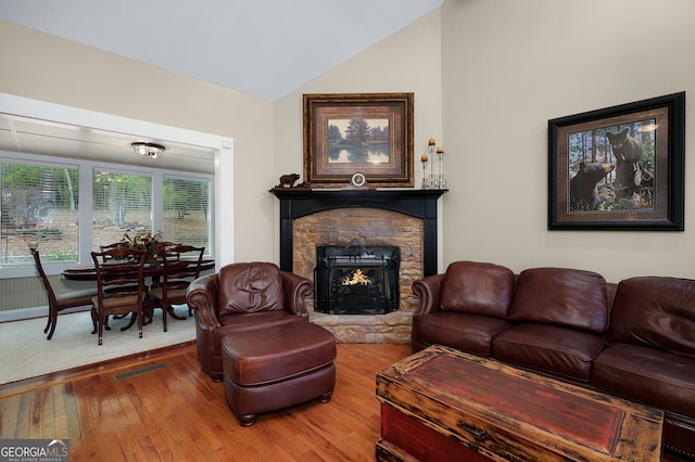 living area featuring lofted ceiling, a stone fireplace, visible vents, and hardwood / wood-style floors