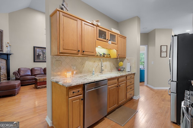 kitchen featuring a sink, stainless steel appliances, decorative backsplash, glass insert cabinets, and light wood-style flooring