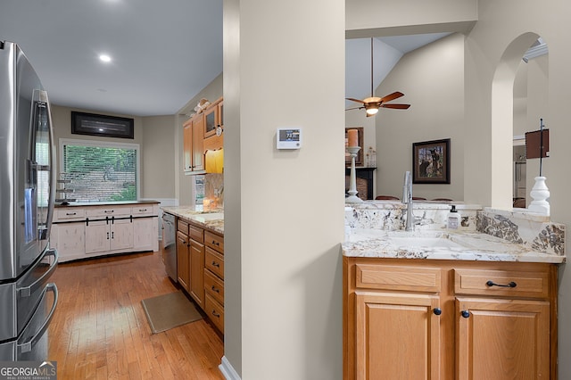 kitchen featuring arched walkways, light wood-style flooring, stainless steel appliances, ceiling fan, and a sink