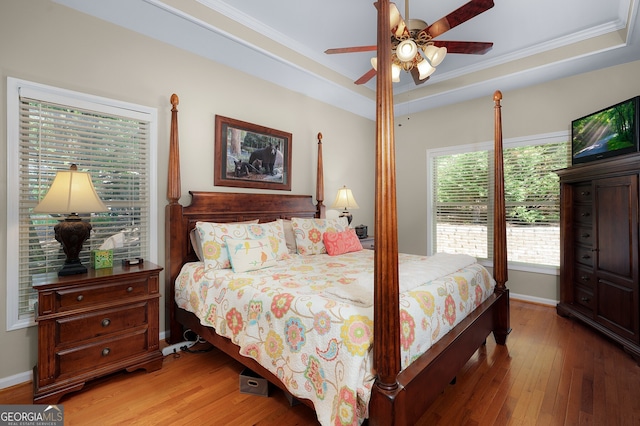 bedroom with wood-type flooring, ornamental molding, a raised ceiling, and baseboards
