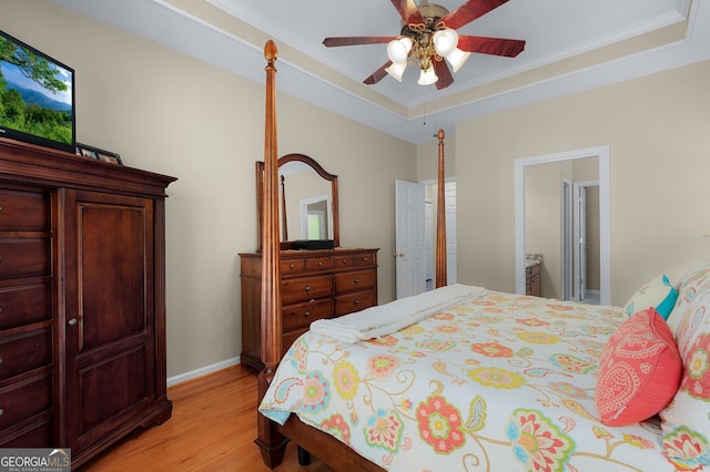 bedroom featuring a raised ceiling, light wood-style flooring, baseboards, and ceiling fan