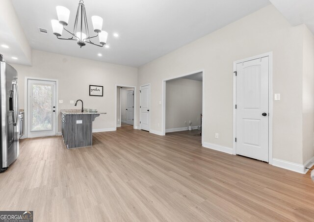 unfurnished living room featuring baseboards, a notable chandelier, light wood finished floors, and visible vents
