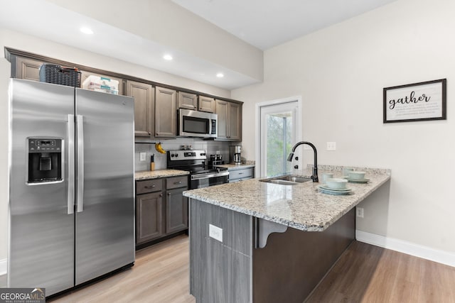 kitchen featuring a peninsula, light wood finished floors, appliances with stainless steel finishes, and a sink