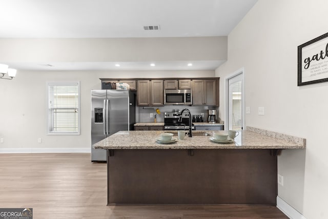 kitchen featuring light wood finished floors, stainless steel appliances, visible vents, light stone counters, and a breakfast bar