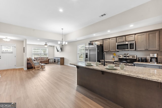 kitchen with a kitchen breakfast bar, stainless steel appliances, visible vents, light wood-style floors, and baseboards